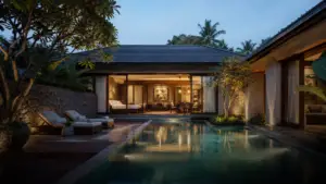 A luxury tropical villa at twilight featuring a glowing rectangular pool, lounge chairs, and open-concept interiors set against lush greenery.